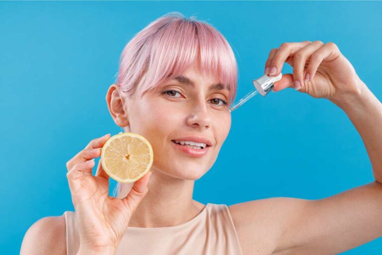 Woman applying vitamin C serum with dropper alongside citrus extract, illustrating antioxidant-rich formulation supporting skin radiance and protection against oxidative stress.